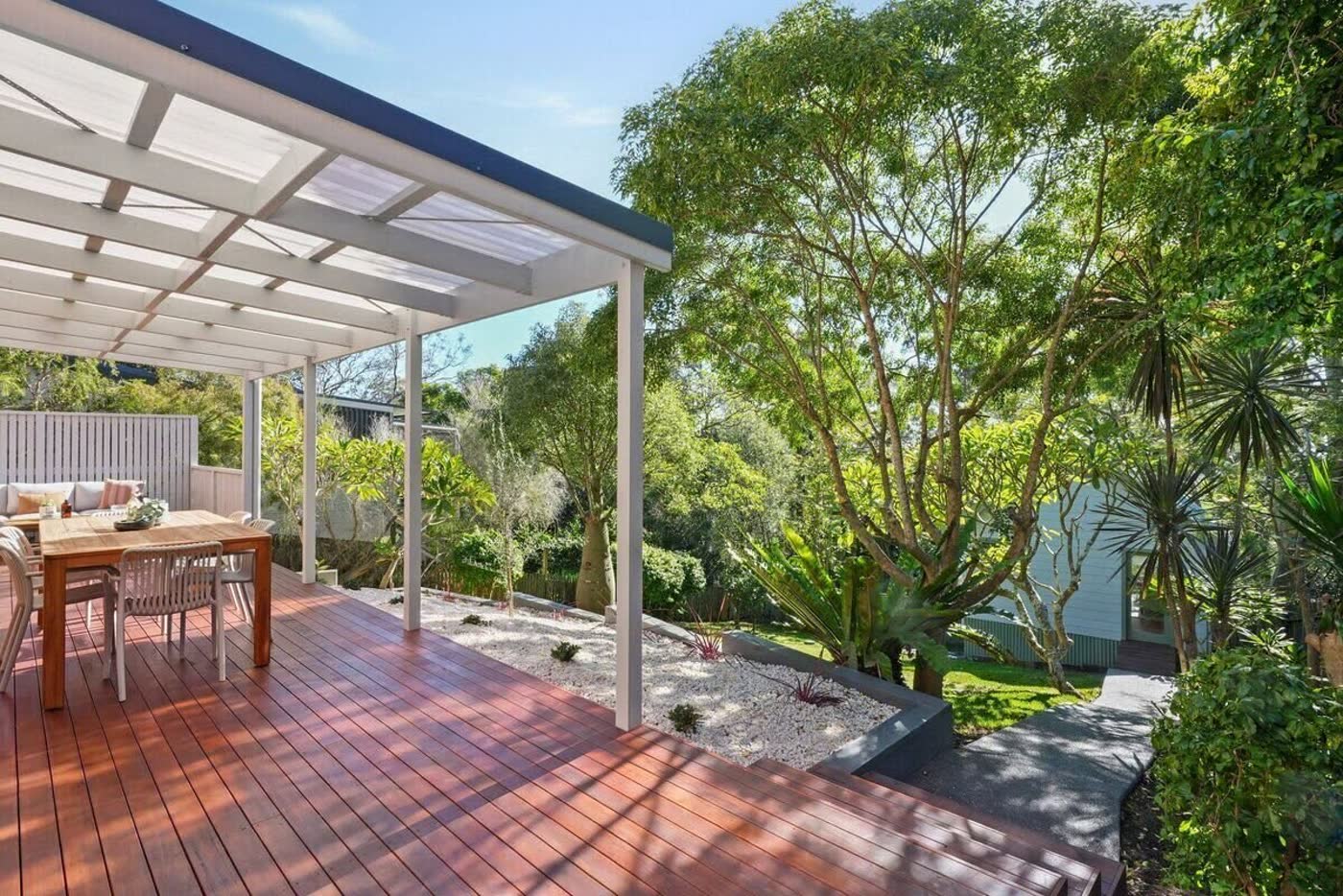 Alfresco timber deck with white pergola overlooking landscaped garden and studio
